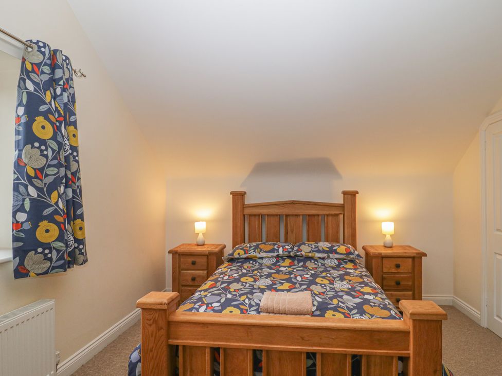 A bedroom with a wooden bed and matching bedside tables with lamps at The Old Barn in Harman's Cross near Swanage
