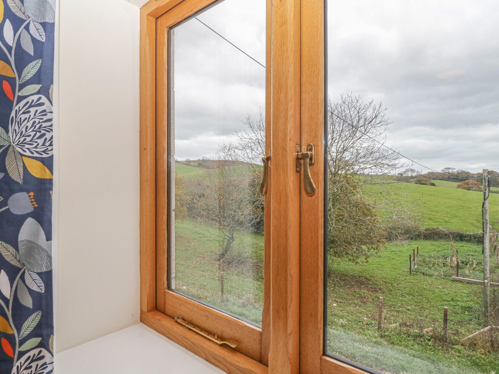 A window with wooden frame looking out to a green field with trees at The Old Barn in Harman's Cross near Swanage
