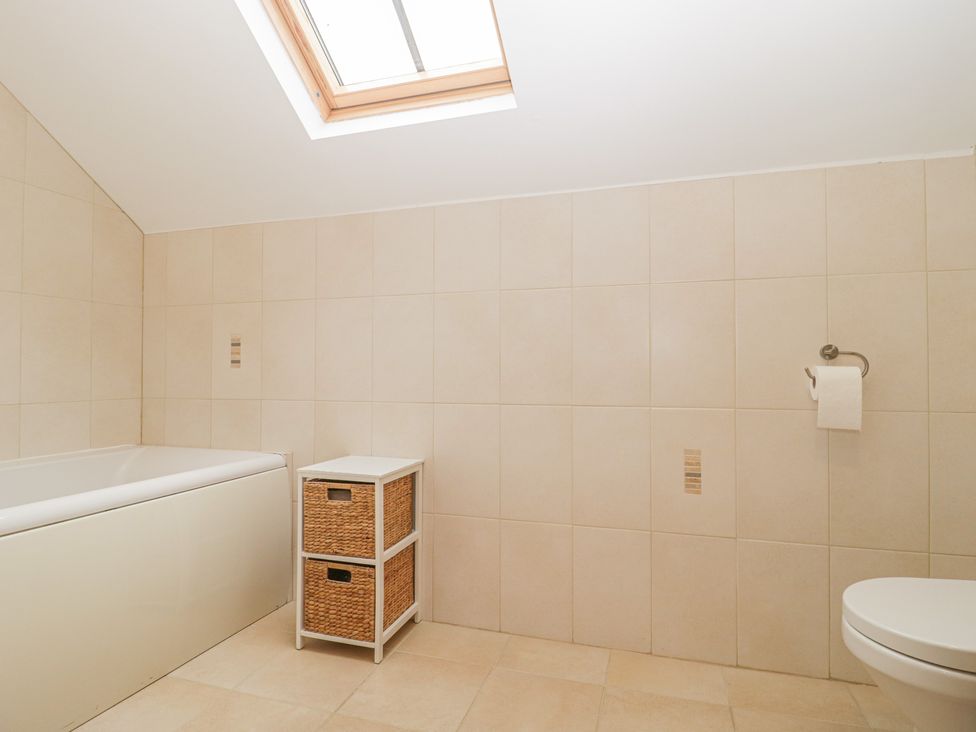 A bathroom with a bathtub a skylight a small storage unit and a toilet at The Old Barn in Harman's Cross near Swanage