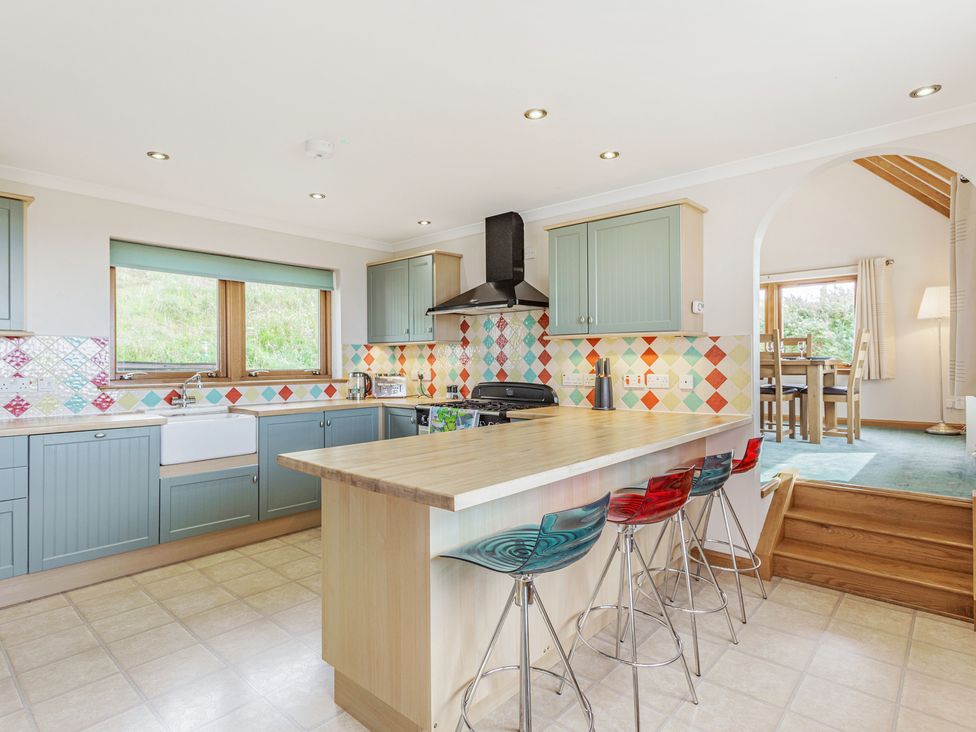 A kitchen with an island and four stools next to a dining area through an archway at Askival in Elgol