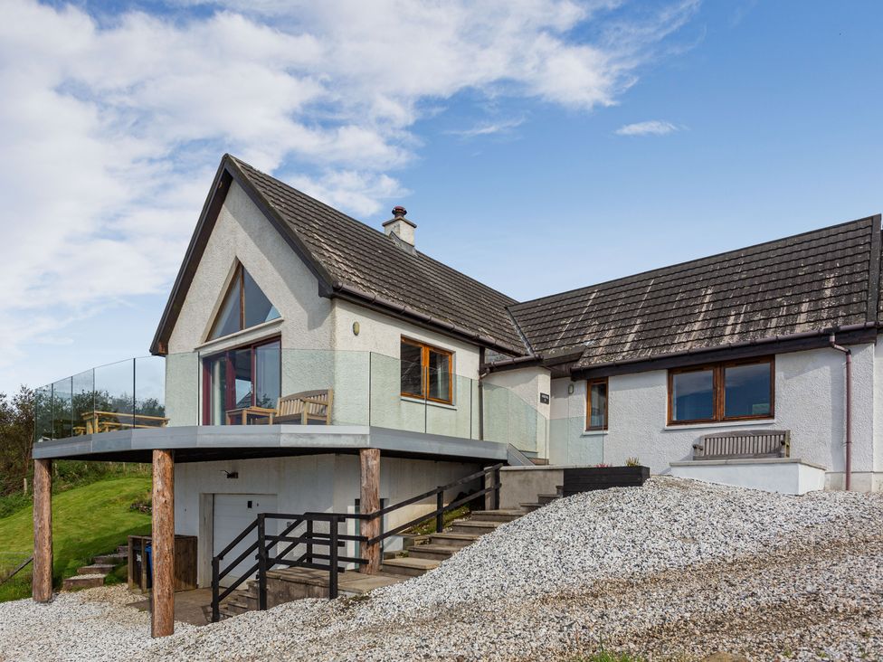A house with a deck supported by wooden posts and stairs leading to a gravel driveway at Askival in Elgol