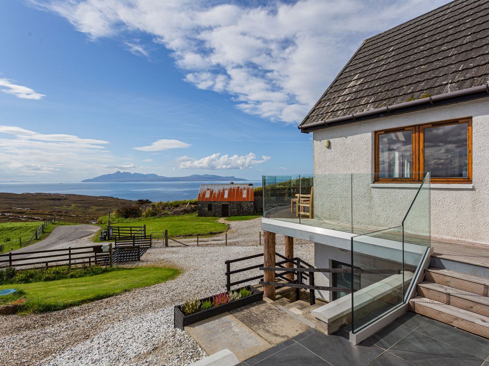 Exterior view of a house with glass balcony overlooking a road grassy area and distant sea at Askival in Elgol