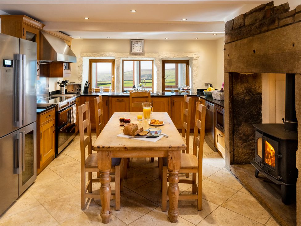 A kitchen with wooden cabinets a wooden dining table and chairs a stainless steel refrigerator and oven and a wood burning stove at The Retreat in Hebden Bridge