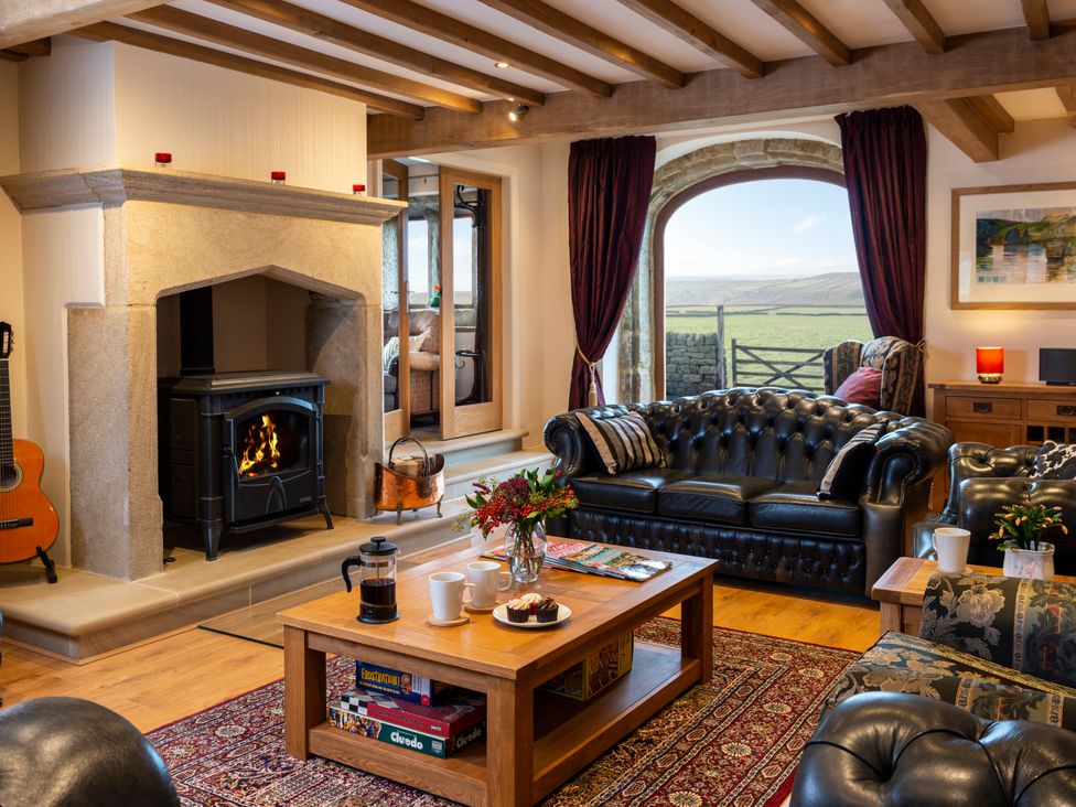 A living room with a stone fireplace a black leather sofa wooden coffee table and a large window with a view at The Retreat in Hebden Bridge