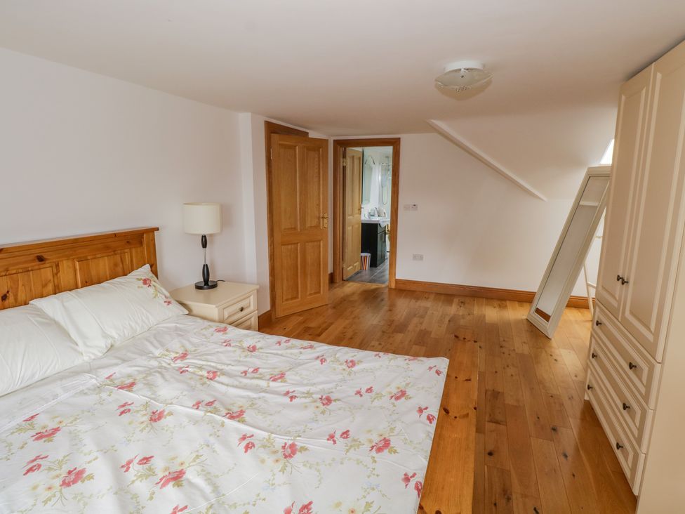 A bedroom with a wooden bed, floral bedspread, bedside table with lamp, wardrobe, and a mirror at Blue Stack House in Meenaguish Beg near Donegal Town County Donegal