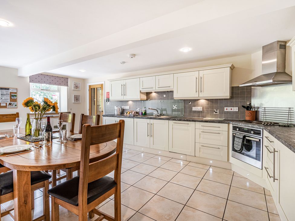 A kitchen with white cabinets wooden dining table and chairs and tiled floor at Hay Barn in Lower Bentham near Ingleton