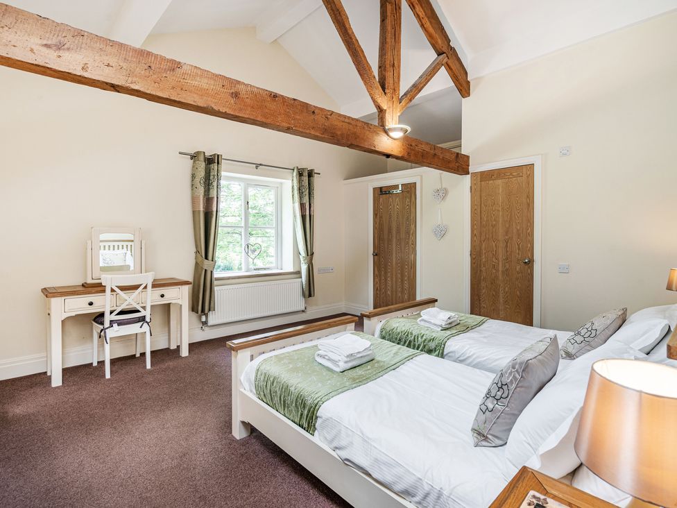 A bedroom with two single beds a dressing table and a window with curtains at Hay Barn in Lower Bentham near Ingleton