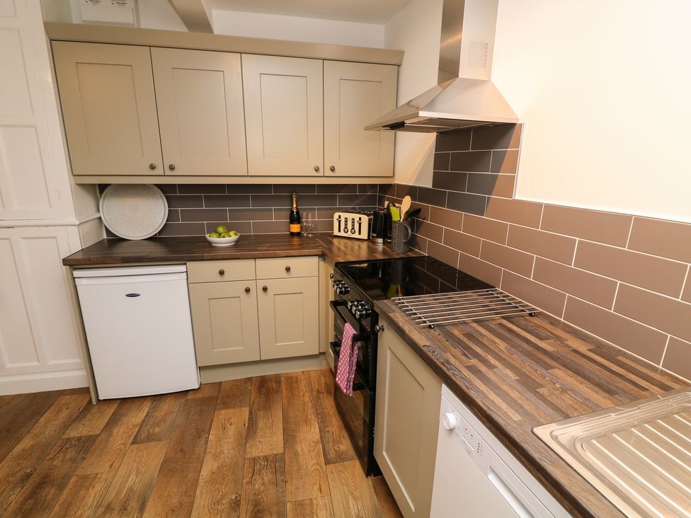 A kitchen with wooden countertops beige cabinets a black stove a small white fridge and a dishwasher at Whitefriars Lodge in Settle