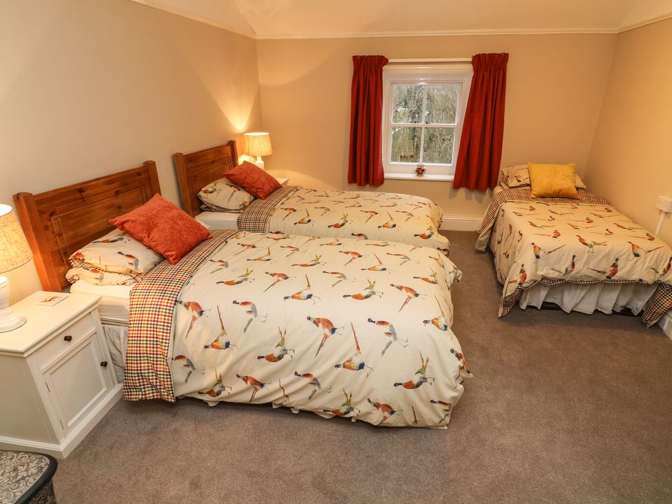 A bedroom with two single beds and one single bed with bird patterned bedding and red curtains at Whitefriars Lodge in Settle