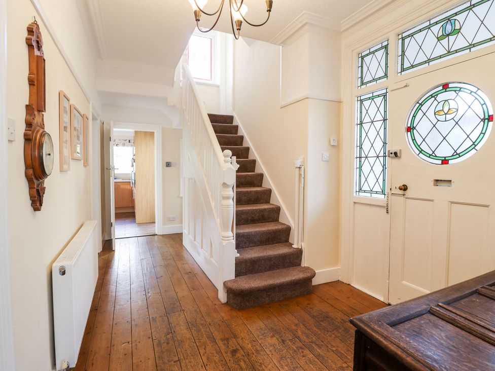 A hallway with wooden flooring a carpeted staircase a door with stained glass and a wall clock at Meadway House in Rhos-on-Sea