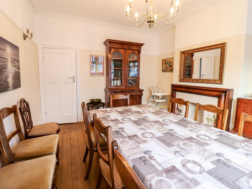 A dining room with wooden chairs a table with a tablecloth and a wooden cabinet at Meadway House in Rhos-on-Sea