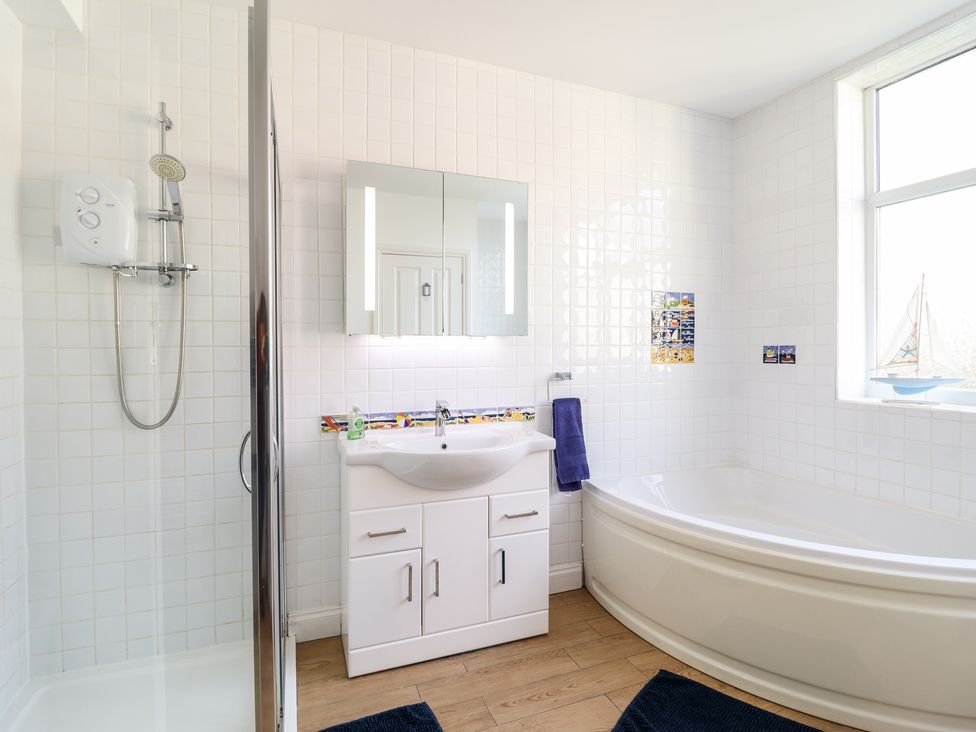 A bathroom with a shower, sink with cabinet, bathtub, and window at Meadway House in Rhos-on-Sea