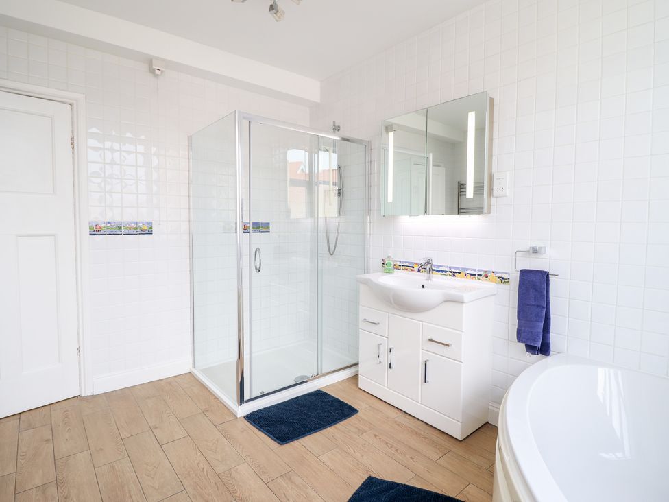A bathroom with a glass shower, white sink cabinet, mirror, towel holder, and wooden floor at Meadway House in Rhos-on-Sea