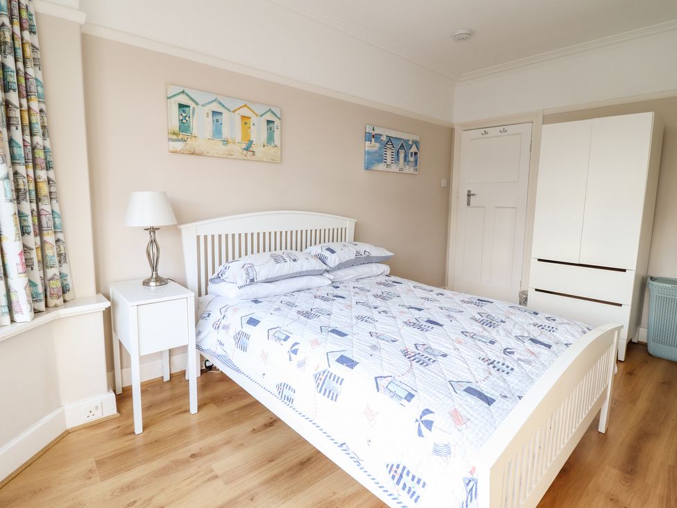 A bedroom with a white bed and bedside table with lamp a white wardrobe and two paintings on the wall at Meadway House in Rhos-on-Sea