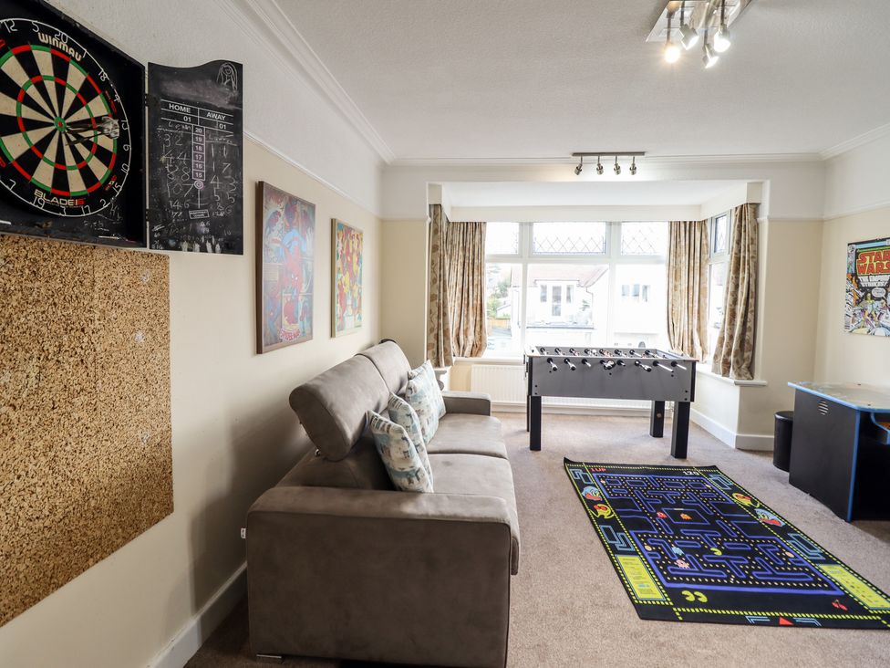 A game room with a gray sofa, foosball table, dartboard, pinball machine, and Pac-Man themed rug at Meadway House in Rhos-on-Sea