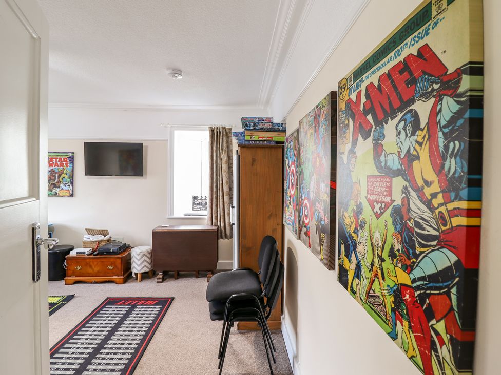 A room with comic book posters on the wall a stack of chairs a wooden cabinet and a television at Meadway House in Rhos-on-Sea