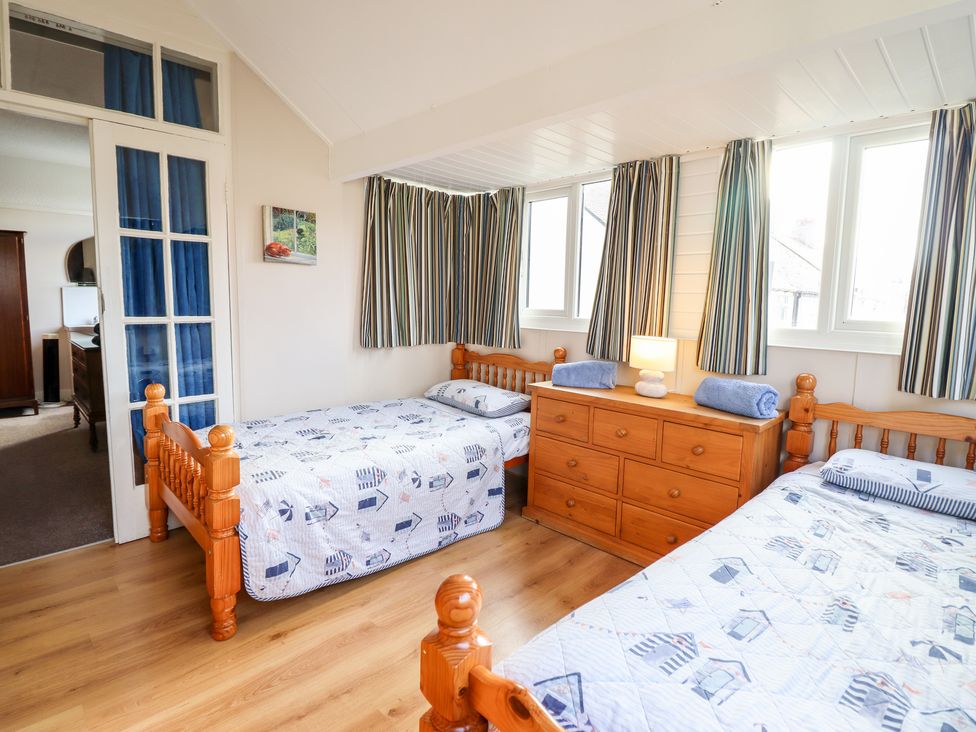 A bedroom with two single wooden beds and a wooden dresser under windows with striped curtains at Meadway House in Rhos-on-Sea