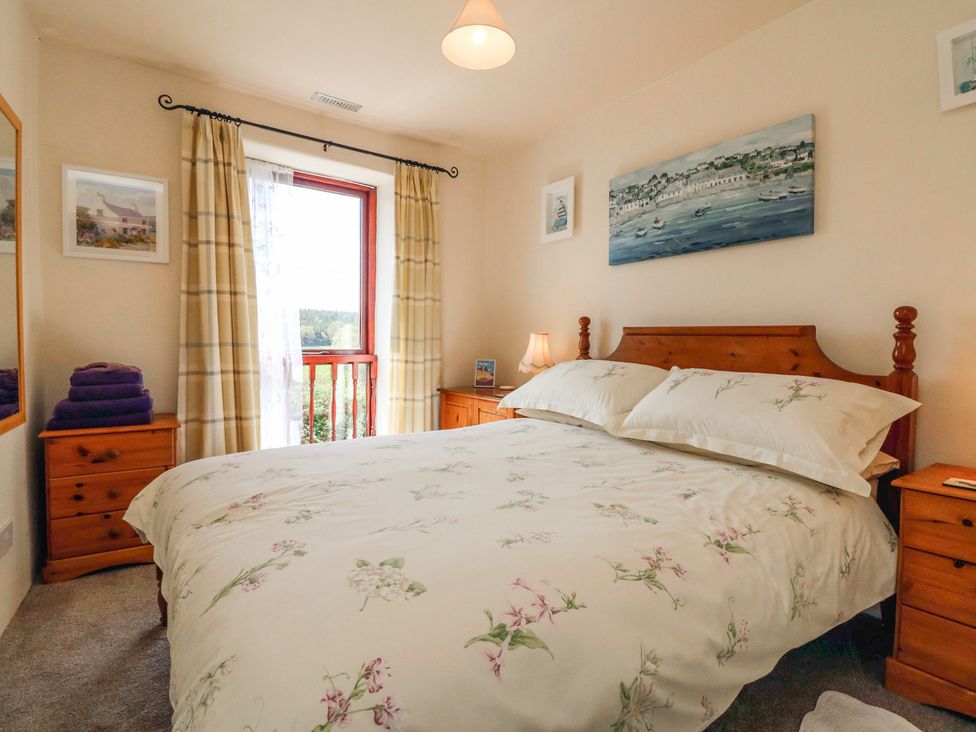 A bedroom with a wooden bed and nightstands beside a window with curtains at Primrose Cottage Huntshaw near Great Torrington