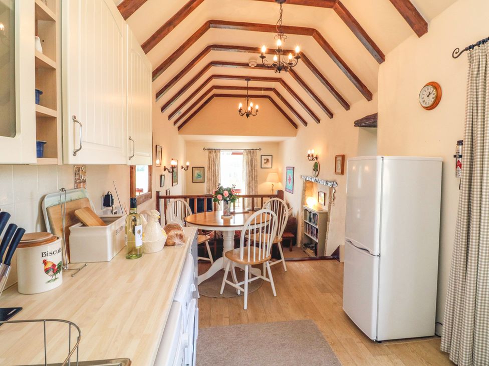 A kitchen and dining area with a round table chairs and a refrigerator at Primrose Cottage in Huntshaw near Great Torrington