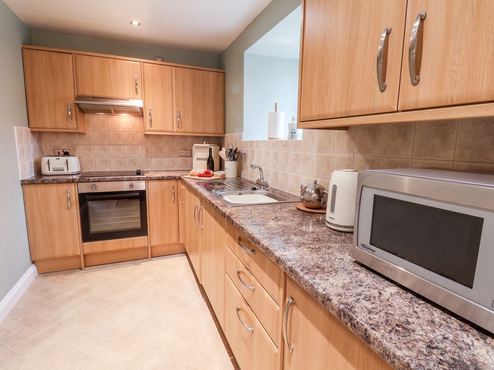A kitchen with wooden cabinets a microwave kettle toaster and an oven at Mulgrave Cottage Dalehouse near Staithes