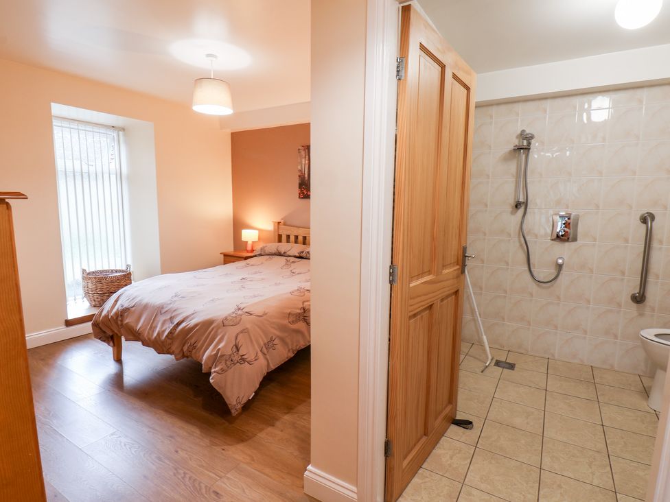 A bedroom with a bed and bedside table next to an open door revealing a tiled bathroom with a shower at Mulgrave Cottage in Dalehouse near Staithes
