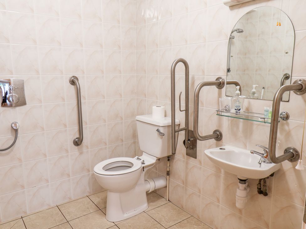 A bathroom with a toilet, sink, mirror, grab bars, and soap dispenser at Mulgrave Cottage in Dalehouse near Staithes