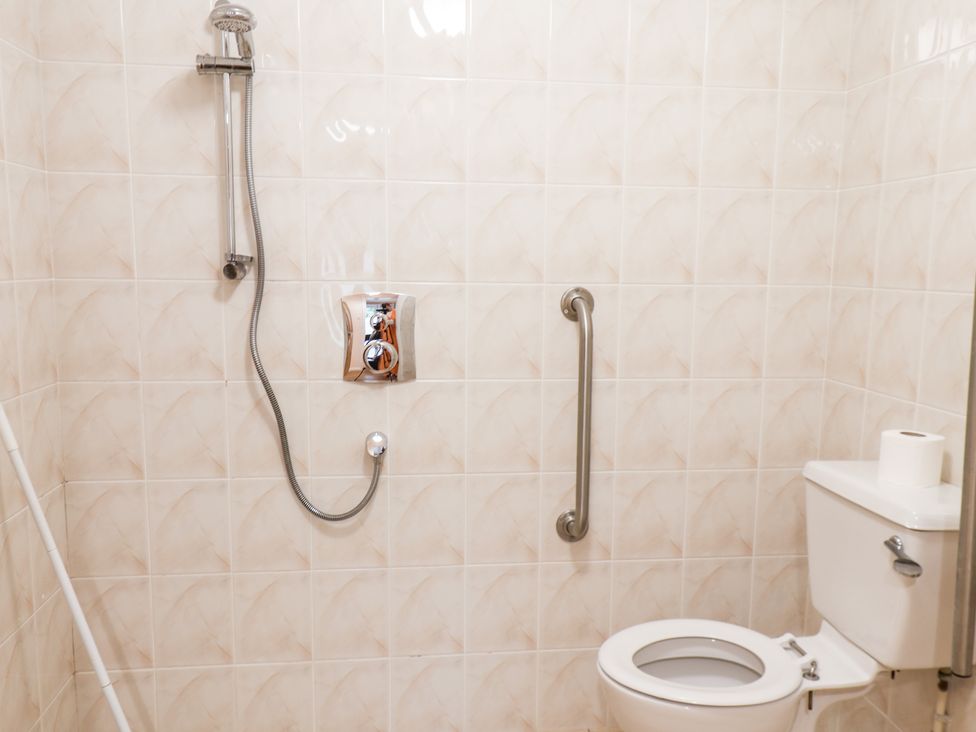 A bathroom with beige tiled walls a white toilet a silver grab bar and a showerhead at Mulgrave Cottage in Dalehouse near Staithes