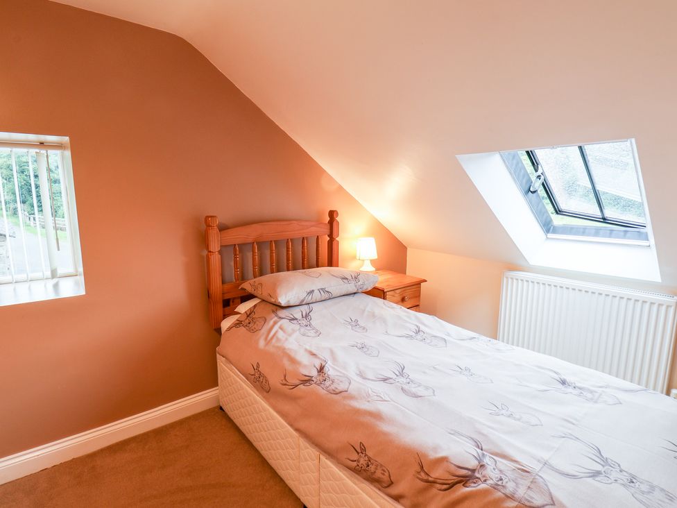 A bedroom with a single bed a wooden headboard a bedside table with a lamp and two windows at Mulgrave Cottage in Dalehouse near Staithes