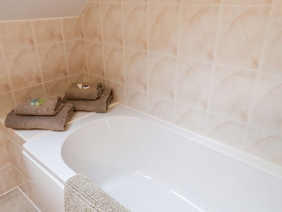 A bathroom with a white bathtub and folded towels placed on the corner at Mulgrave Cottage in Dalehouse near Staithes