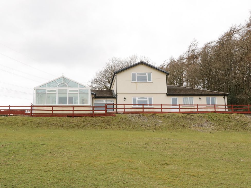 A two-story house with large windows and a glass conservatory surrounded by a red wooden fence at Bryn Derw Holiday Cottage in Eglwysbach near Llanrwst and Conwy