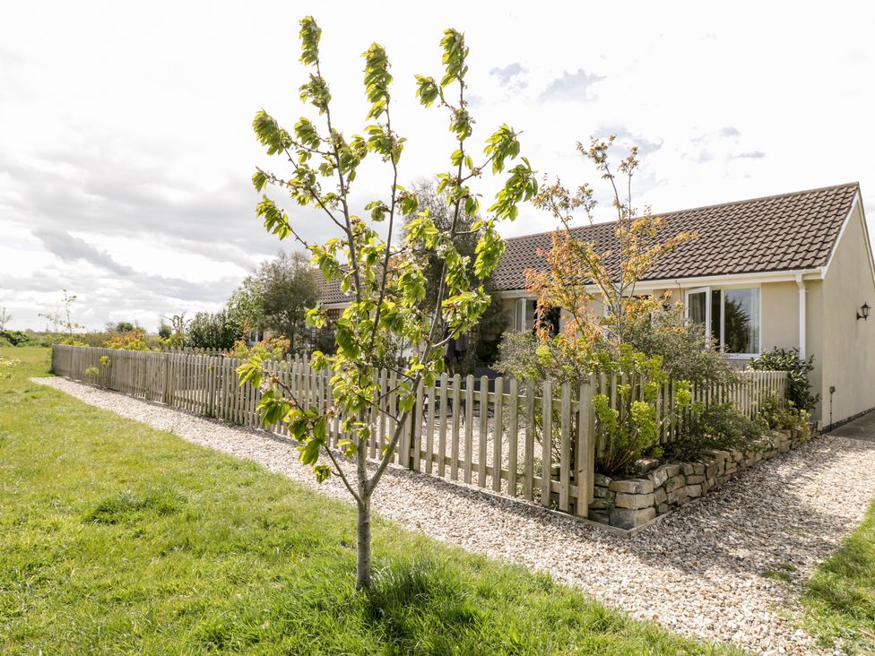 A single-story house with a tiled roof surrounded by a wooden fence and garden at Teal in Watchfield near Highbridge