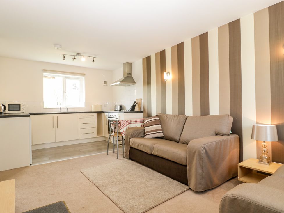 An open plan living area with a sofa a lamp and a kitchen with cabinets in Teal Watchfield near Highbridge