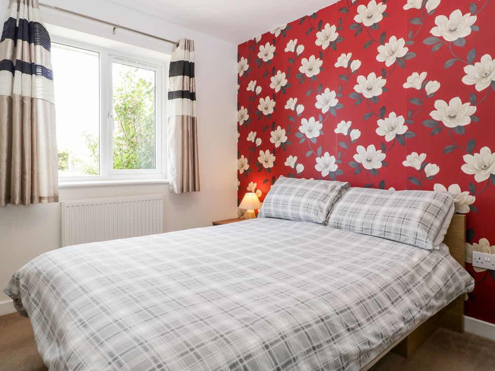 A bedroom with a double bed with plaid bedding a bedside table with a lamp and floral wallpaper at Teal Watchfield near Highbridge