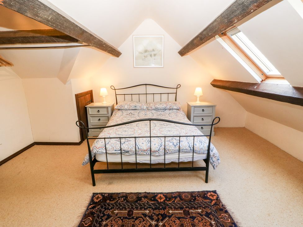 A bedroom with a double bed and bedside tables with lamps under a slanted ceiling with exposed wooden beams at Bwthyn y Dderwen Oak Cottage in Pwllheli