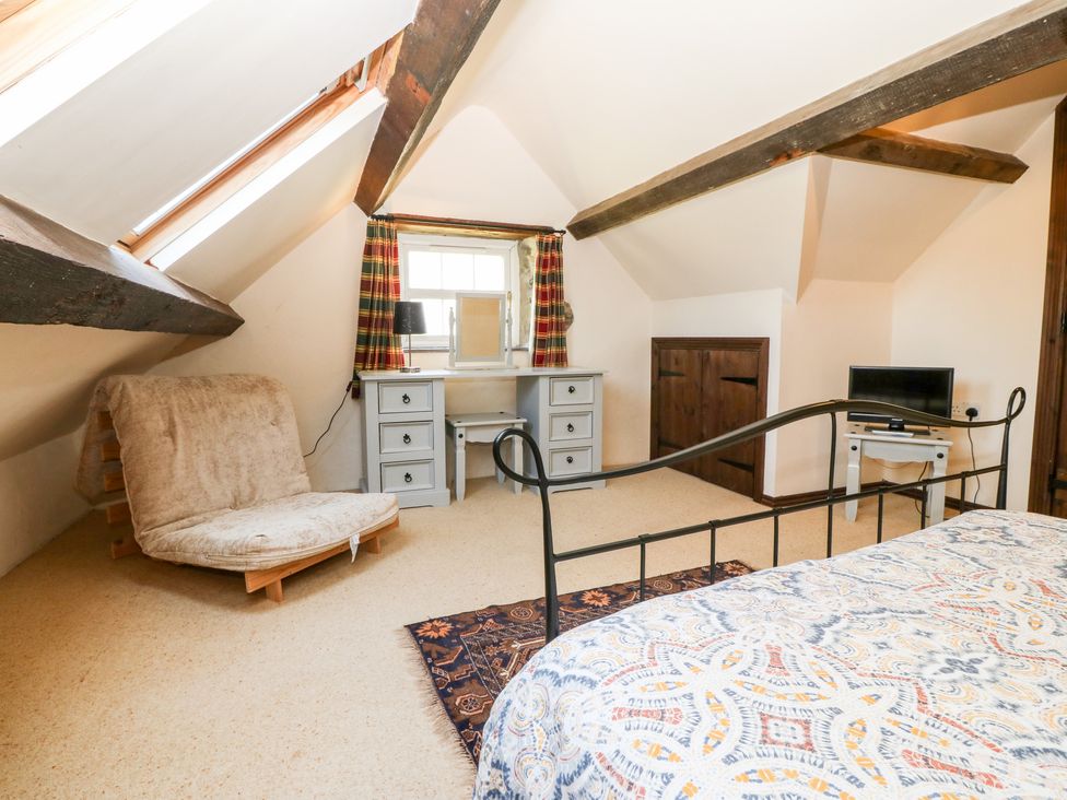 A bedroom with a metal bed frame a wooden chair a desk with a mirror and a small table with a TV at Bwthyn y Dderwen Oak Cottage in Pwllheli