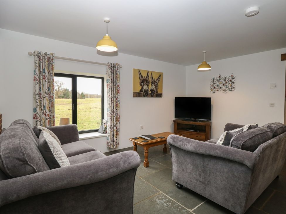 A living room with two grey sofas a wooden coffee table a television and a window with patterned curtains at Tricker's Cottage in Morton on the Hill near Lenwade