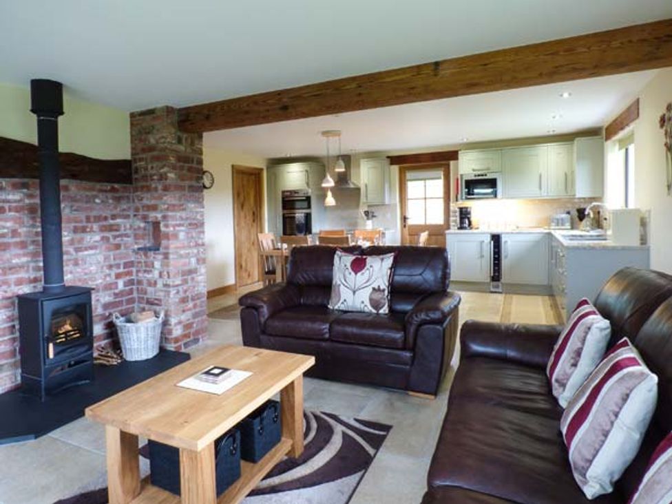 An open living room and kitchen with leather sofas wooden coffee table and brick fireplace at Tyn Y Celyn Uchaf in Clocaenog near Ruthin