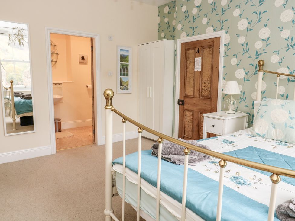 A bedroom with a metal bed frame a wardrobe nightstand with a lamp and an open door leading to a bathroom at Fern House in Kettlewell
