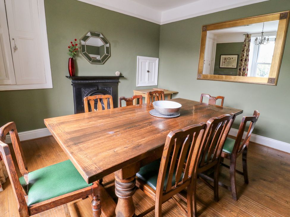 A dining room with a wooden table and chairs a bowl on the table a fireplace with a red vase a mirror and a large framed mirror on the walls at Fern House in Kettlewell