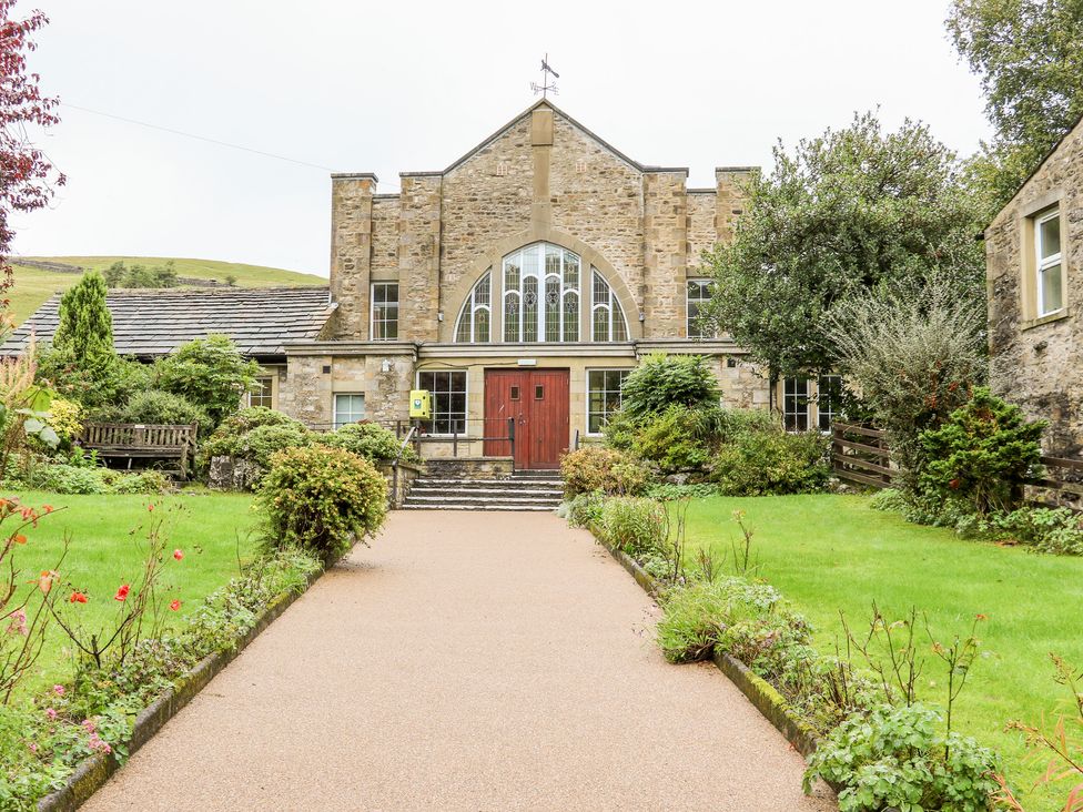 A stone building with large arched windows and red doors surrounded by greenery at Fern House in Kettlewell
