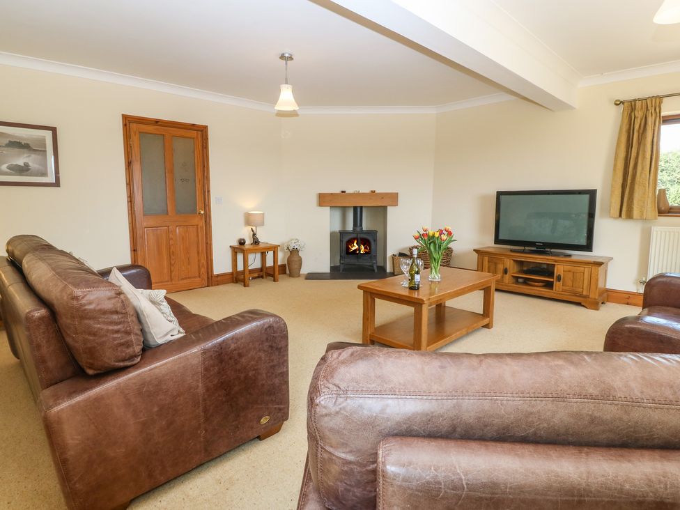 A living room with brown leather sofas a wooden coffee table a television on a wooden stand a fireplace and a wooden door at Fferam Y Llyn in Rhosgoch near Cemaes Bay