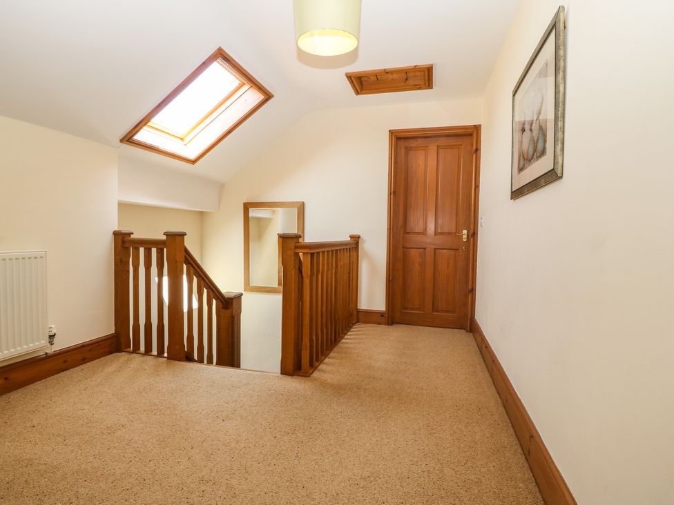A hallway with wooden railing, a skylight, a wooden door, a mirror, and a framed picture at Fferam Y Llyn in Rhosgoch near Cemaes Bay