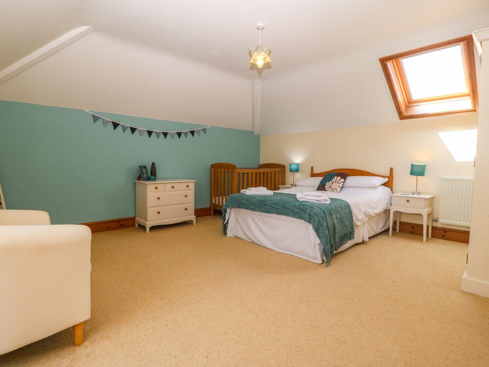 A bedroom with a bed a crib a chest of drawers and an armchair at Fferam Y Llyn in Rhosgoch near Cemaes Bay