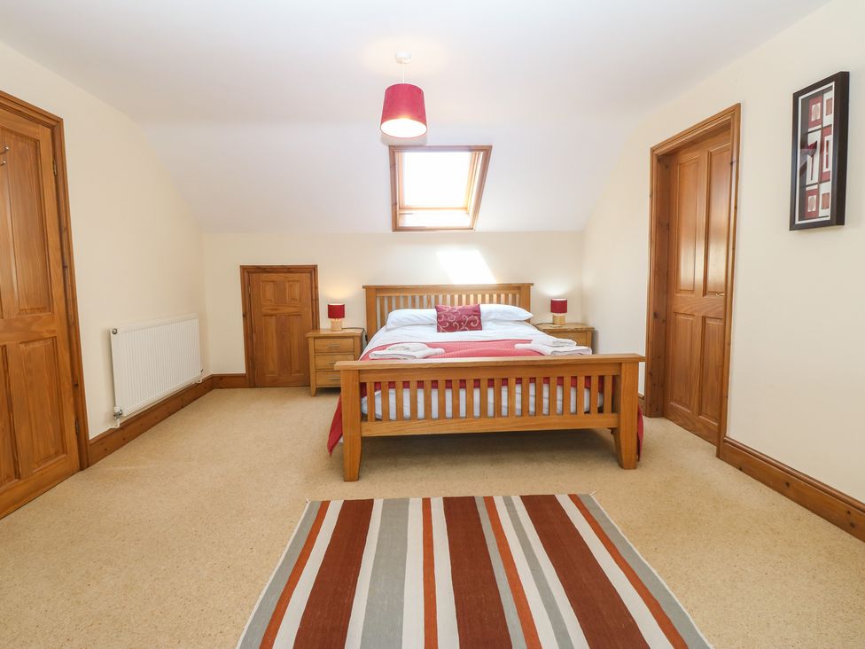 A bedroom with a double wooden bed two bedside tables with lamps and a striped rug at Fferam Y Llyn in Rhosgoch near Cemaes Bay