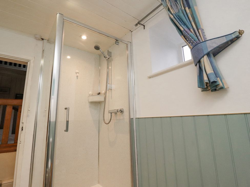 A bathroom shower cubicle with a glass door next to a window with a curtain at Haworth Barn in Stainforth near Settle