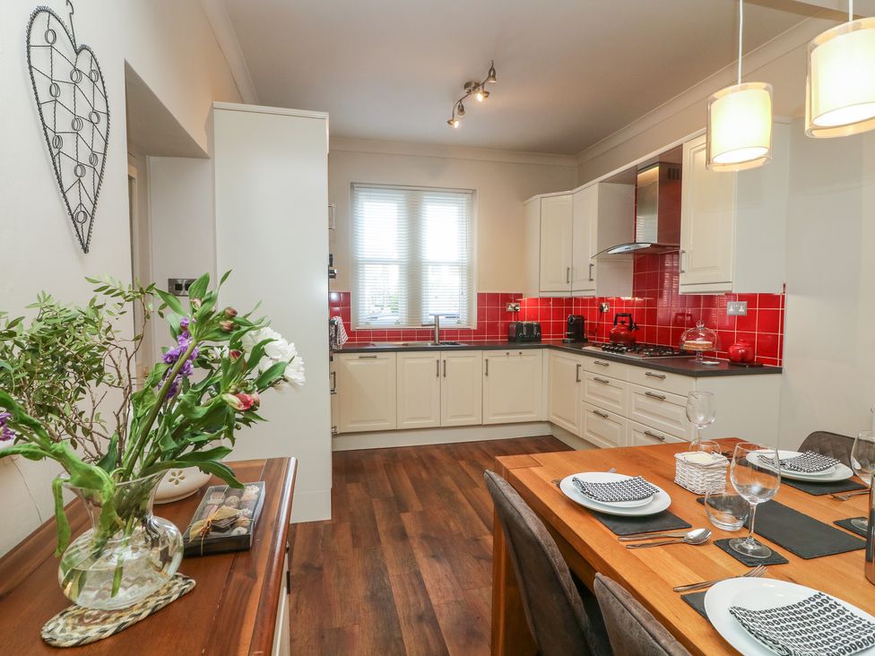 A kitchen with white cabinets red tile backsplash a wooden dining table set with plates and glasses at Lonsdale Cottage in Kirkby Lonsdale