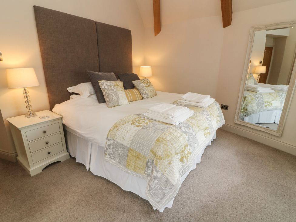 A bedroom with a bed a bedside table with lamp and a wall mirror at Lonsdale Cottage in Kirkby Lonsdale