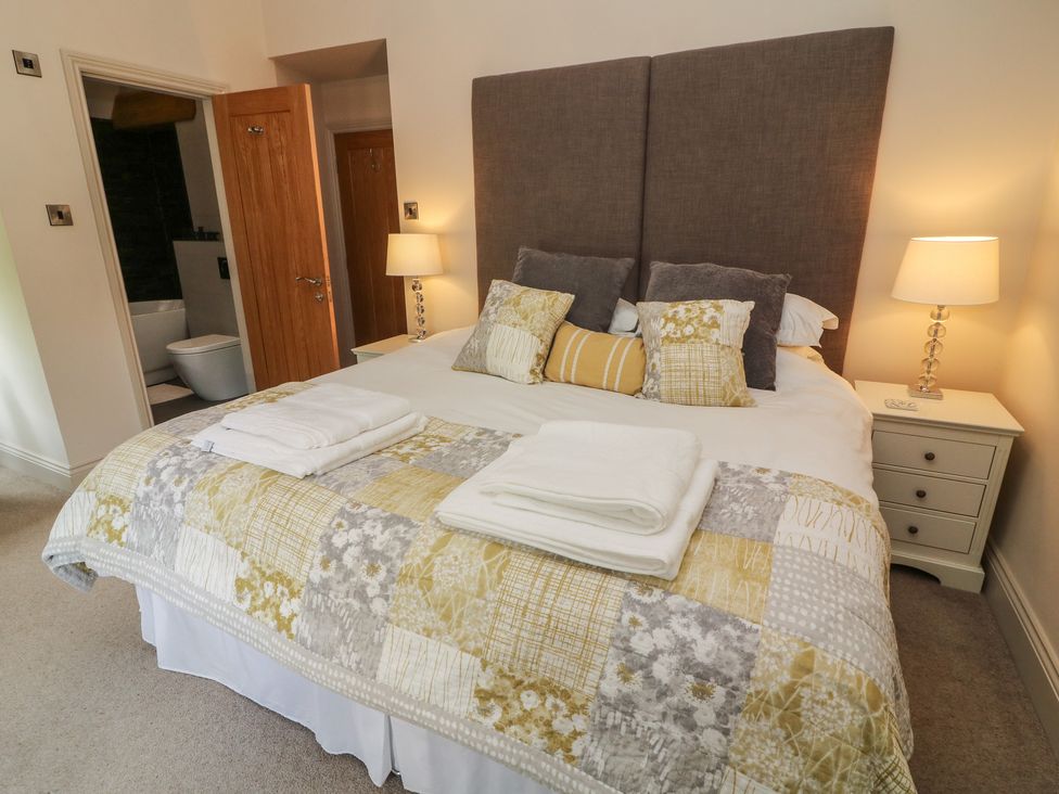 A bedroom with a double bed bedside tables with lamps and an open door showing a bathroom at Lonsdale Cottage in Kirkby Lonsdale