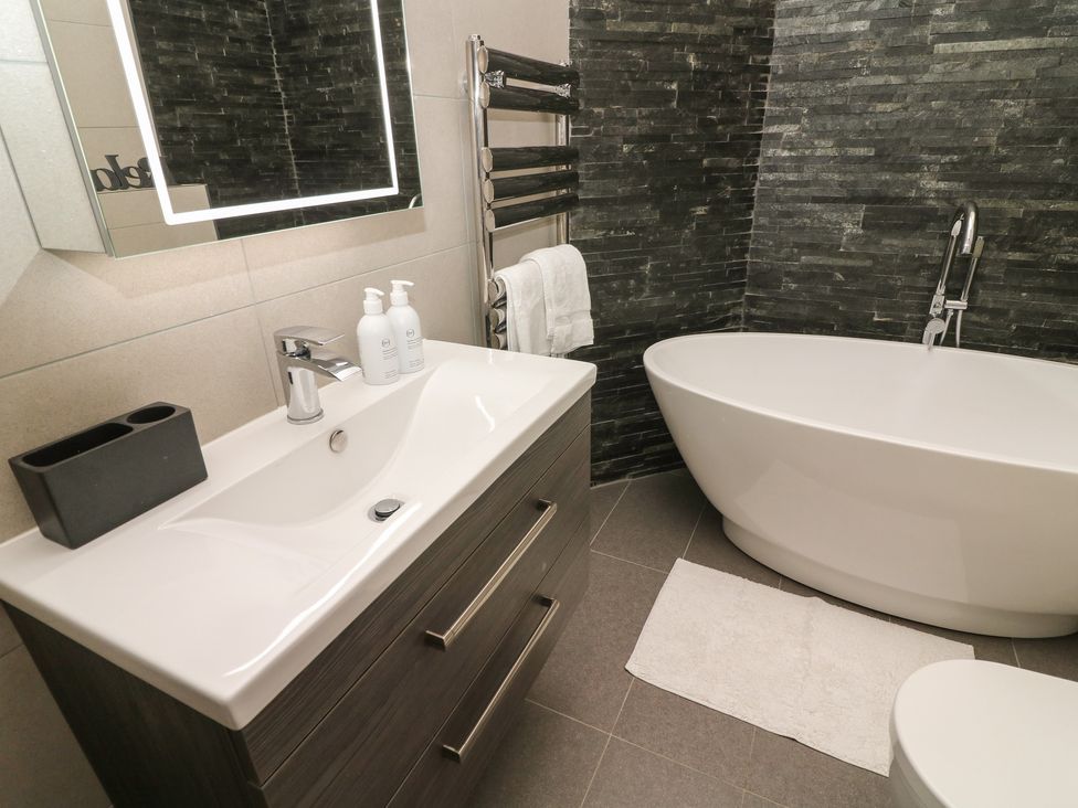 A bathroom with a white bathtub and sink with cabinet and a towel on a rail at Lonsdale Cottage in Kirkby Lonsdale