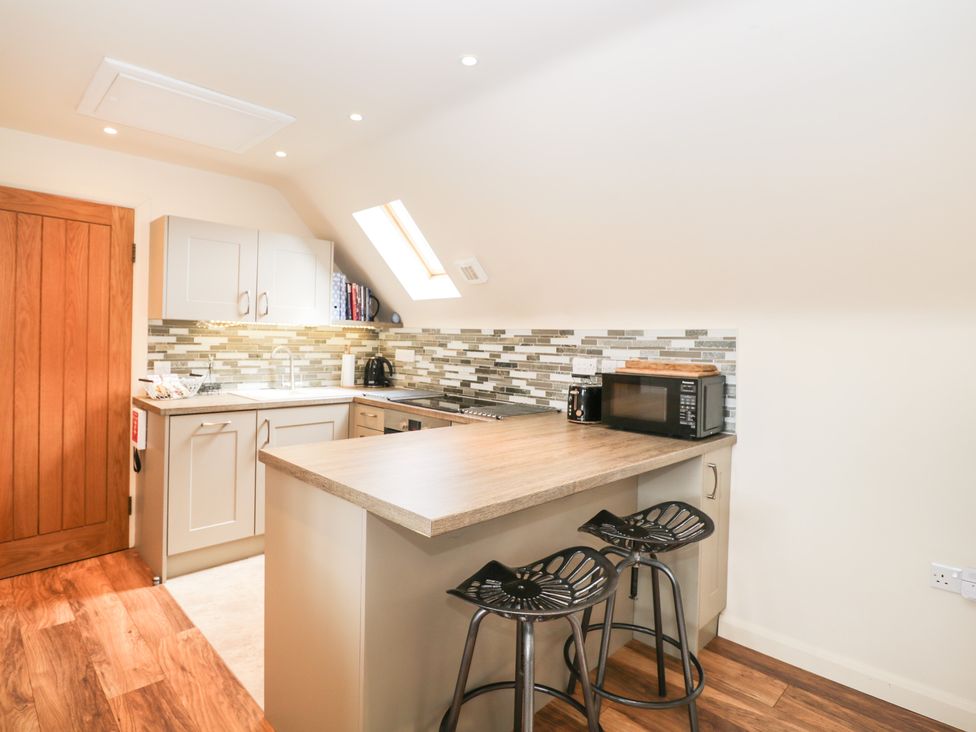 A small kitchen with a wooden countertop, two black stools, a microwave, a kettle, and white cabinets at Shephard's Retreat in Charlton Mackrell near Somerton